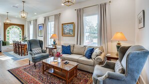 A well-lit living room with a sofa, armchairs, a coffee table, and a dining area with a chandelier and curtains.