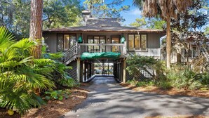 A house with a covered porch, a staircase leading to the entrance, and a pathway surrounded by greenery.