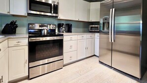 Una cocina moderna con electrodomésticos de acero inoxidable, armarios blancos y suelo de madera clara.