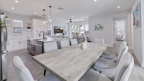 Une cuisine moderne avec des meubles blancs, un îlot central et un coin repas comprenant une longue table et des chaises.