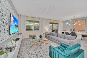 Una sala de estar moderna con un sofá, una mesa de centro y un televisor. Hay un comedor con una mesa y sillas.