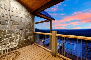 A wooden deck with a hanging chair, a stone wall, and a view of a pool and landscape.