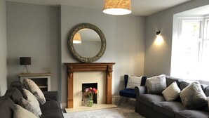 Een woonkamer met een open haard, twee banken, een spiegel en een lamp.