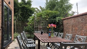 Een terras met een houten tafel en stoelen, een fles champagne en een bloemenvaas.