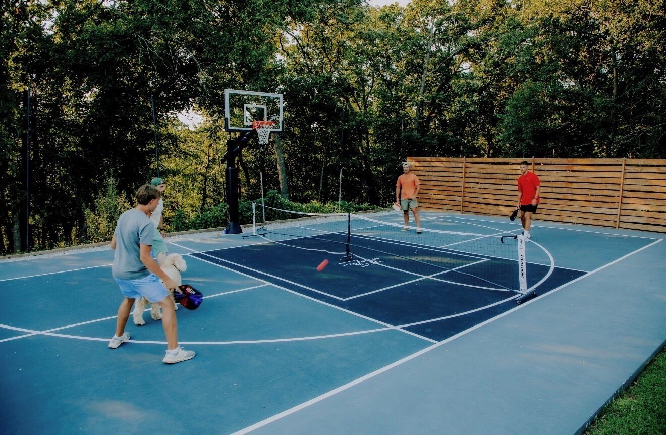 An outdoor basketball court with a wooden fence and trees in the background.