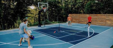 An outdoor basketball court with a wooden fence and trees in the background.
