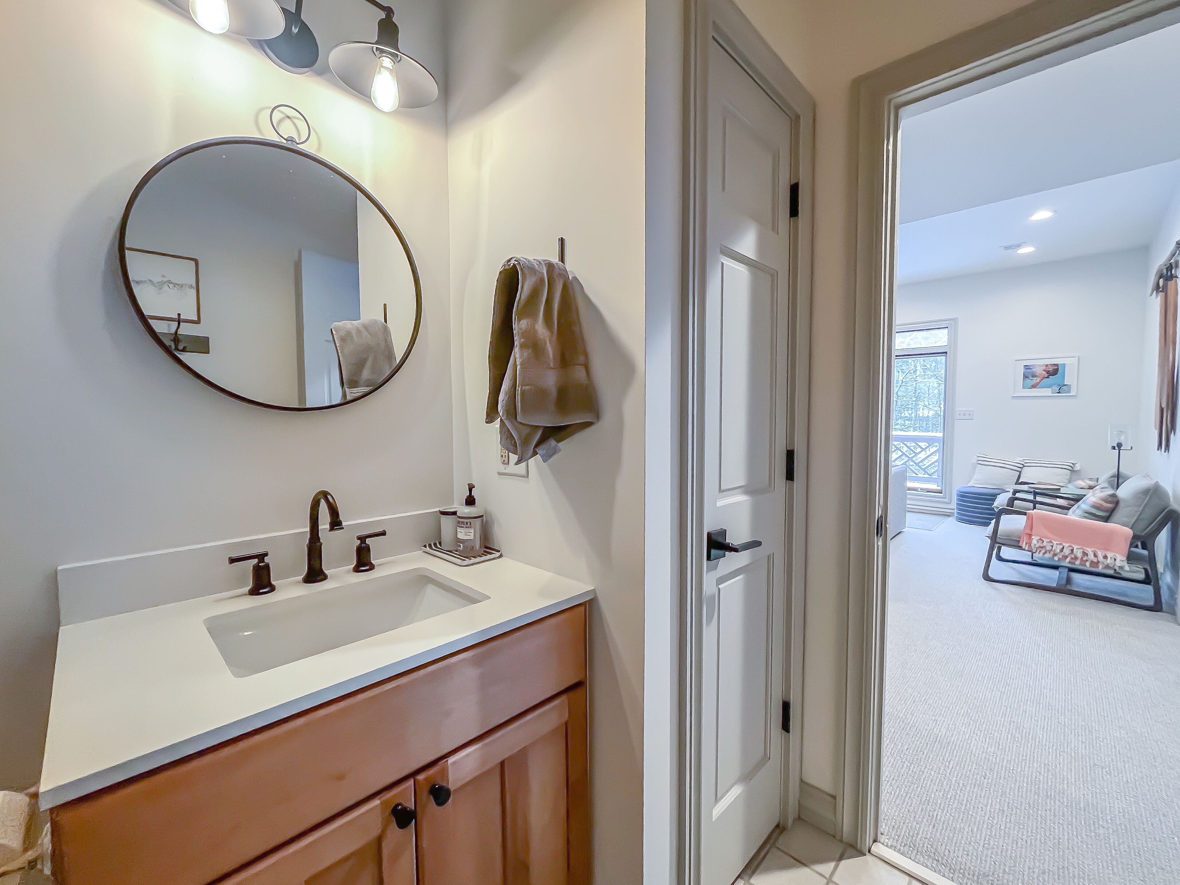 Une salle de bain avec un lavabo blanc, un miroir rond et une serviette accrochée au mur.