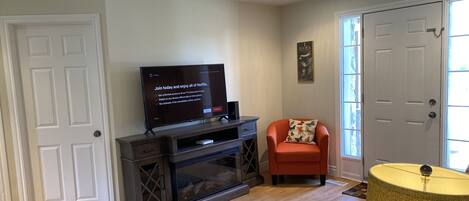 A living room with a flat-screen TV, a red armchair, a patterned rug, and a lamp.