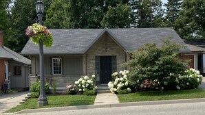 Une maison à deux étages avec une façade en pierre, un toit sombre et un porche à l’avant orné de fleurs blanches.