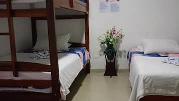 A dormitory room with bunk beds, a small table with a vase of flowers, and an air conditioning unit on the wall.