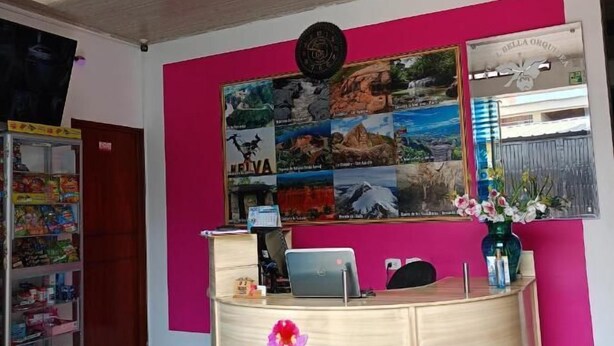 A reception desk with a laptop, a clock, and a framed collage of images on the wall behind it. - Hotel Bella Orquidea (Neiva)