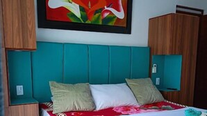 A bed with a white bedspread and teal headboard, a colorful painting above, and wooden cabinets. - Hotel Bella Orquidea (Neiva)