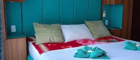 A bed with a white bedspread and teal headboard, a colorful painting above, and wooden cabinets.