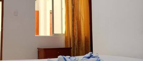 A hotel room with a bed, a television mounted on the wall, and a window with curtains.