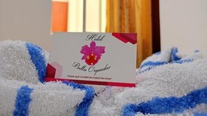 A hotel room with a bed, a card on the bed, and a TV in the background. - Hotel Bella Orquidea (Neiva)