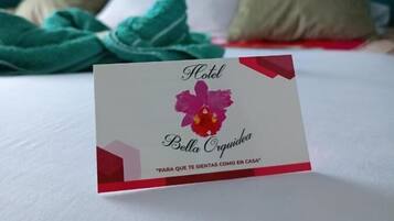 A hotel room with a teal headboard, a bed with white bedding, and a card on the bed.