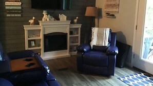 A living room with a fireplace, a television mounted above it, and a blue armchair. - Lakefront Property 
Fish, Cook and EAT!
Swim, Float, Relax (Sparta)