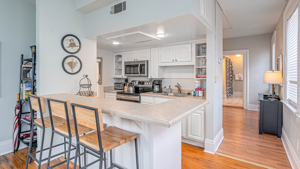 A modern kitchen with white cabinetry, a central island with bar stools, a microwave, and a coffee maker. - Location! Perfect Downtown Savannah Couples Getaway 1 bed 1 bath (Savannah)