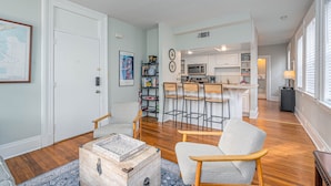 A spacious living room with a wooden coffee table, a patterned armchair, and a kitchen area with a bar and white cabinets. - Location! Perfect Downtown Savannah Couples Getaway 1 bed 1 bath (Savannah)