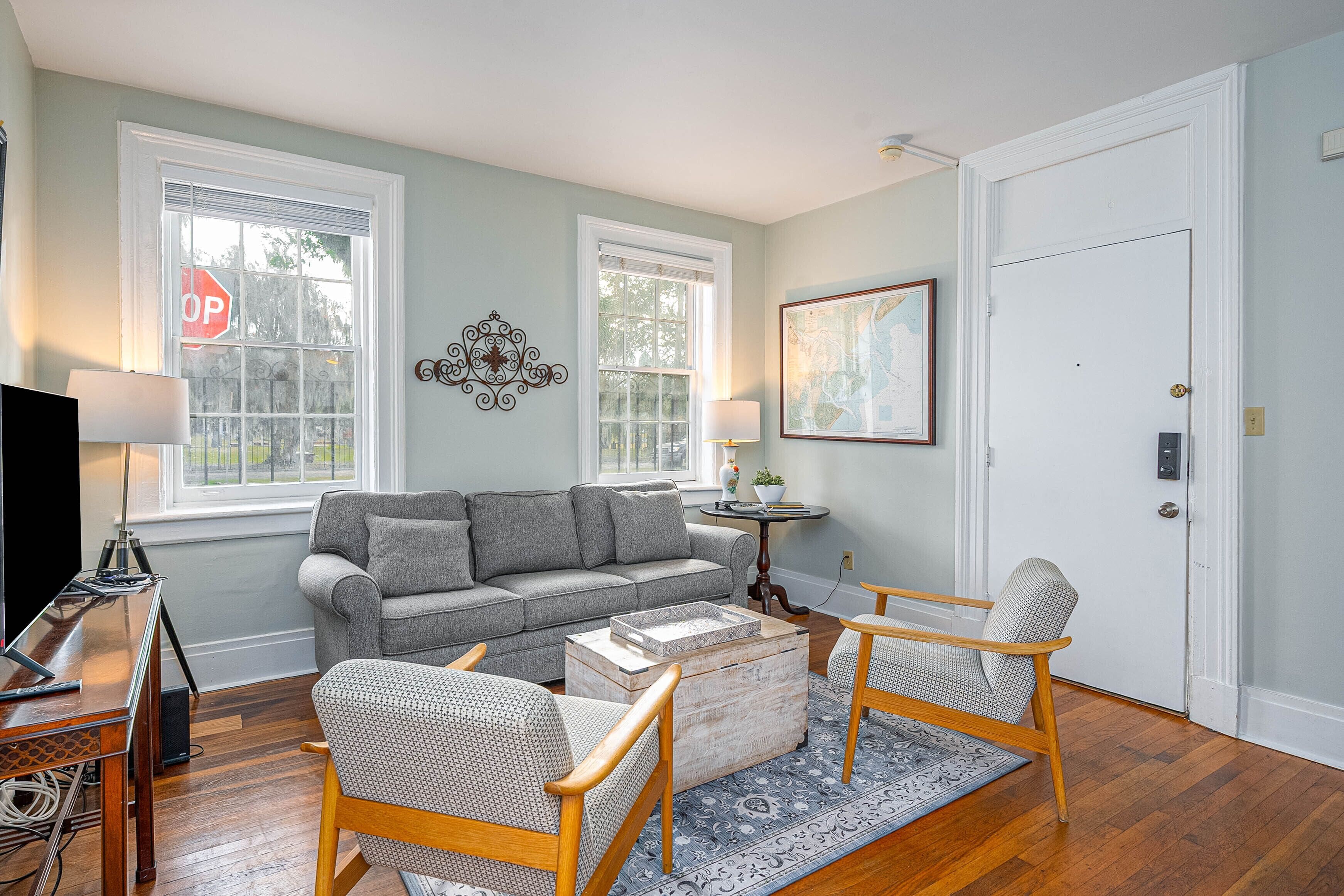 A living room with a gray sofa, two wooden chairs, a coffee table, and a TV on a wooden stand.