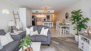 A modern living room with a gray sofa, a coffee table, and a dining area with white chairs. - Oceanfront Resort - Hot Tub, Heated Pool, Balcony (Murrells Inlet)