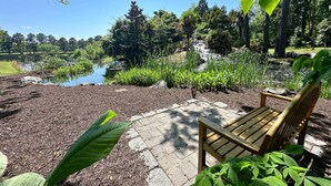 Eine Holzbank in einem Garten mit Teich und Bäumen.