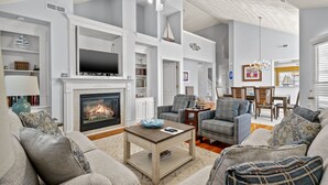 Ein geräumiges Wohnzimmer mit Kamin, moderner Möblierung und einem Fernseher.
