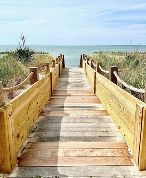 Un muelle de madera que conduce a una playa con vista despejada al océano.