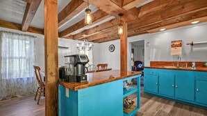 A kitchen with a blue countertop, wooden beams, and a coffee machine. - Windsor House | 3BR Historic Island Retreat, King Suite, Grill + Near Shops & Dining (Chincoteague Island)