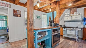 A kitchen with wooden beams, a vintage stove, and a blue island with baskets. - Windsor House | 3BR Historic Island Retreat, King Suite, Grill + Near Shops & Dining (Chincoteague Island)