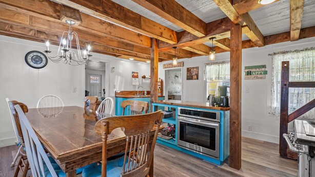 A rustic kitchen with wooden beams, a dining area with a large wooden table and chairs, and a blue accent wall. - Windsor House | 3BR Historic Island Retreat, King Suite, Grill + Near Shops & Dining (Chincoteague Island)