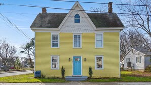 A yellow house with a blue door, white trim, and a small porch. - Windsor House | 3BR Historic Island Retreat, King Suite, Grill + Near Shops & Dining (Chincoteague Island)