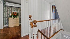 A staircase with white balusters and a wooden handrail, leading to a room with a dresser and a mirror. - Windsor House | 3BR Historic Island Retreat, King Suite, Grill + Near Shops & Dining (Chincoteague Island)