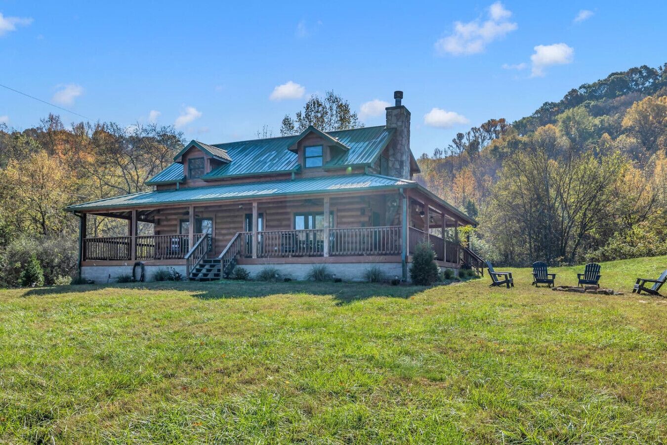 A log cabin with a porch and a chimney, surrounded by a grassy field and trees.
