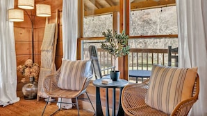A cozy room with wooden walls, two wicker chairs with striped cushions, a small round table, and a potted plant.