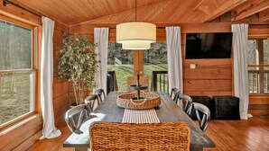 A wooden cabin dining area with a table, chairs, a hanging lamp, and a view of the outdoors.