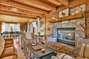 A cozy log cabin interior with a stone fireplace, wooden furniture, and a dining area.