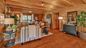 A cozy log cabin interior with a large sofa, a wooden dining table, and a fireplace.