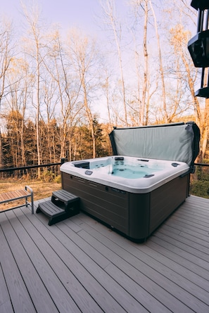 Un jacuzzi en una terraza de madera con vistas a árboles sin hojas.