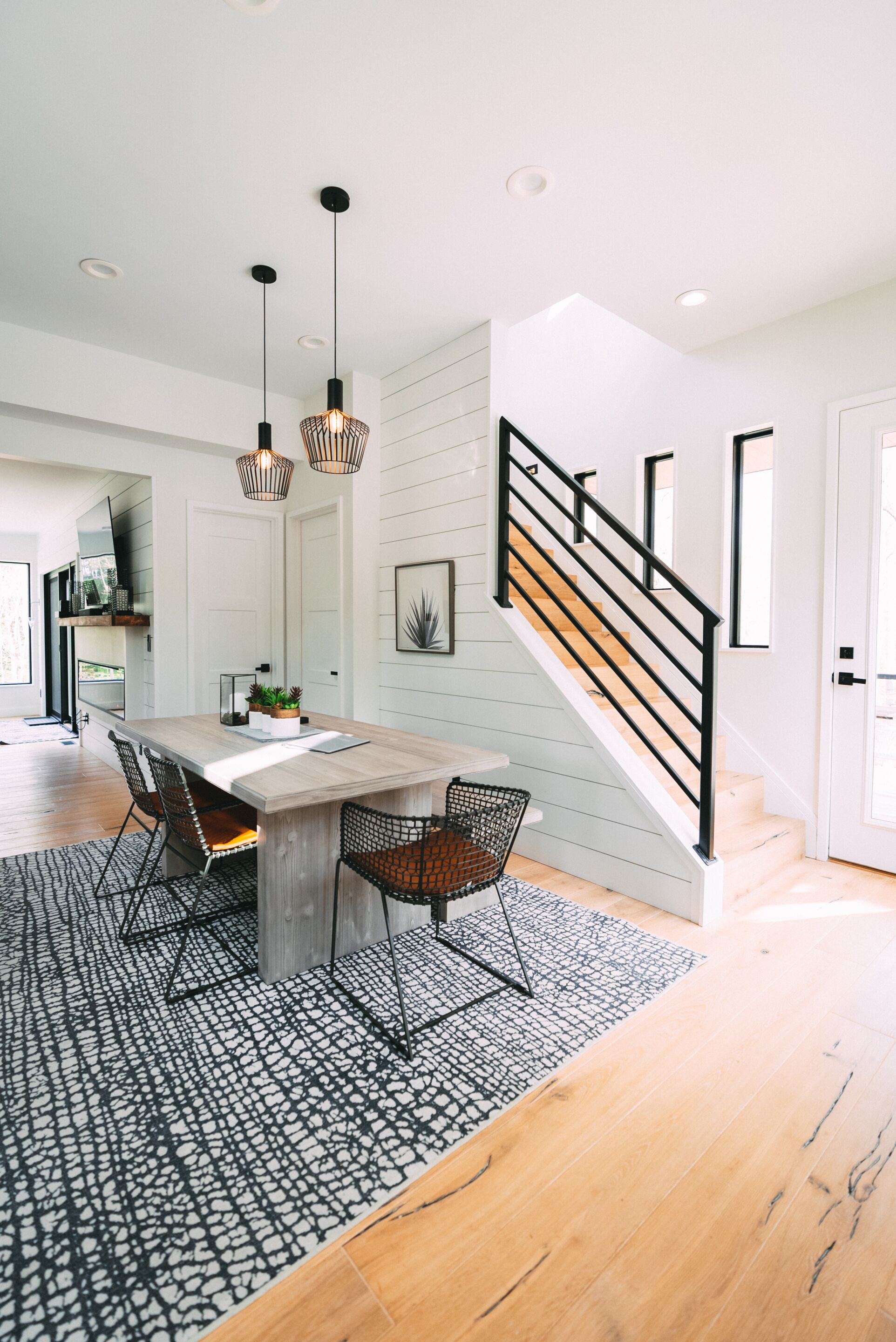 A modern kitchen with a central island, pendant lighting, and a staircase with a black railing.