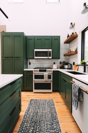 A compact kitchen with green cabinets, a microwave, a stove, and a sink.