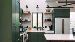 Una cocina moderna con armarios verdes, encimera blanca y suelo de madera.