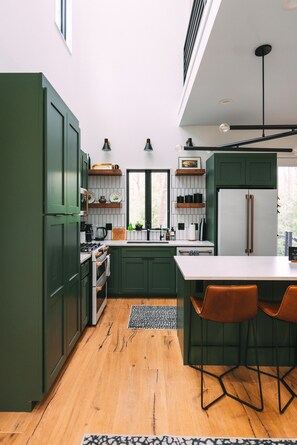 Une cuisine moderne avec des meubles de couleur verte, un plan de travail blanc et un plancher en bois.