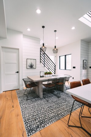 A modern dining area with a wooden table, black wire chairs, and a patterned rug.