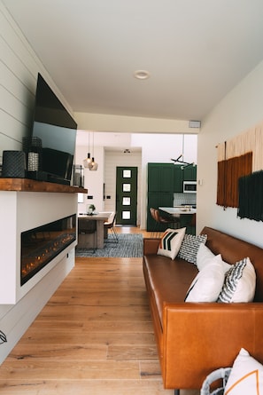 Una sala de estar moderna con chimenea, un sofá de cuero marrón y un comedor al fondo.