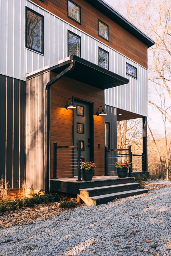 A modern house with a wooden front door, a covered porch, and a gravel driveway.