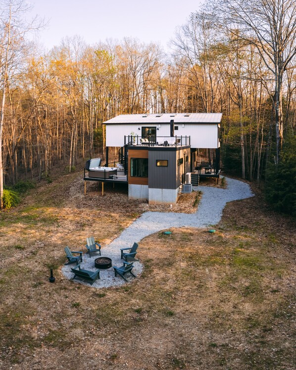 A modern cabin with a deck, outdoor seating, and a fire pit.