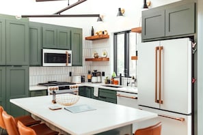 Una cocina moderna con armarios verdes, encimeras blancas, un refrigerador blanco y una isla central con asientos.