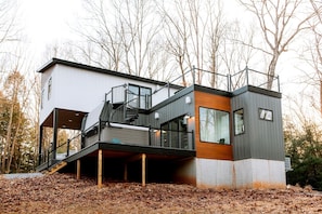 A modern multi-story house with a staircase leading to a balcony, surrounded by trees.
