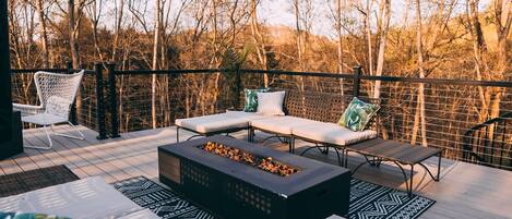 An outdoor deck with lounge seating, a fire pit, and a view of leafless trees.